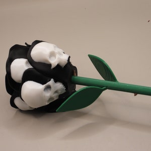May include: A black rose with white skull-shaped petals and a green stem. The rose is a unique and decorative item.