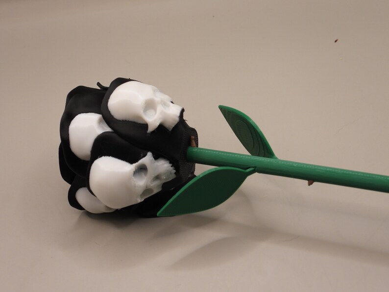 May include: A black rose with white skull-shaped petals and a green stem. The rose is a unique and decorative item.