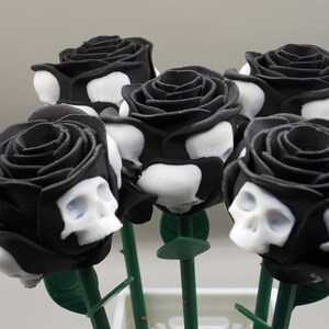 May include: A bouquet of six black roses with white skull designs. The roses are arranged in a vase and have green stems.