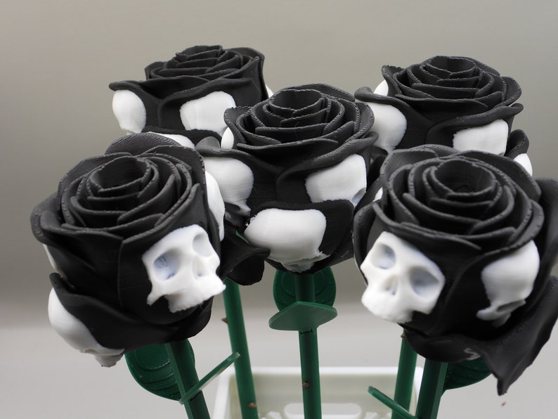 May include: A bouquet of six black roses with white skull designs. The roses are arranged in a vase and have green stems.