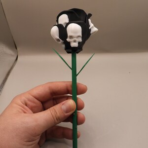 May include: A black and white skull rose with green leaves. The rose is made of plastic and is about 10 inches tall.