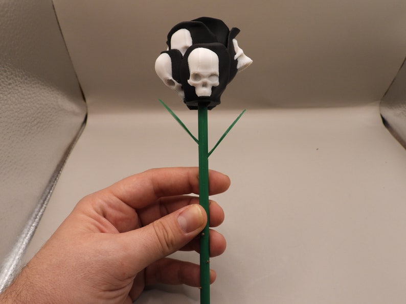 May include: A black and white skull rose with green leaves. The rose is made of plastic and is about 10 inches tall.