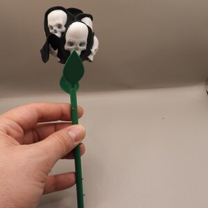 May include: A black and green rose with a cluster of white skulls at the top.