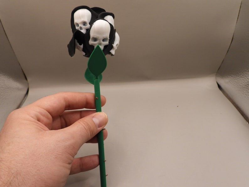 May include: A black and green rose with a cluster of white skulls at the top.