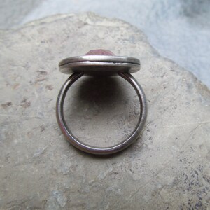 May include: A silver ring with a pink gemstone set in a bezel setting. The ring is on a gray background.