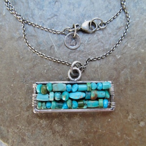 May include: A silver-toned necklace featuring a rectangular pendant frame filled with three horizontal rows of small, irregular turquoise-colored beads. The pendant hangs from a delicate silver-toned chain with a lobster clasp and a small round tag.