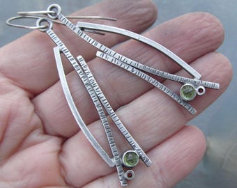 May include: Silver earrings with a geometric design and green gemstones. The earrings have a textured finish and are dangle style.