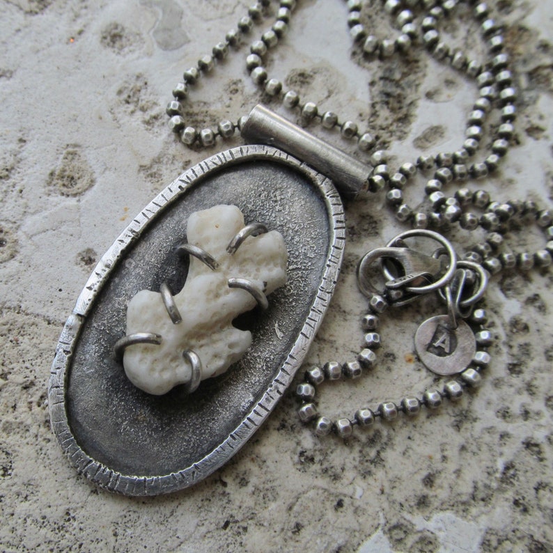 May include: A silver pendant necklace with a white coral piece set in a silver oval. The pendant is attached to a silver chain with a silver clasp.