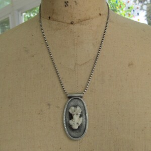 May include: A silver chain necklace with an oval pendant featuring a white fossilized piece of coral.