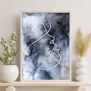 May include: A framed abstract art print with a white line drawing of a face on a black and gray background with gold accents.