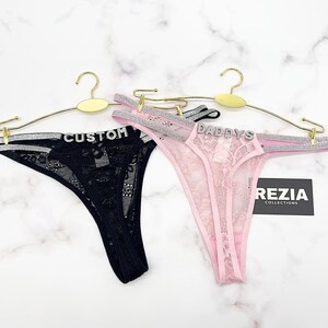 May include: Two thong panties made of floral lace, one black and one light pink. Each features double silver glitter straps on the sides and a silver rhinestone word across the front waistband. The black pair reads CUSTOM and the pink pair reads DADDYS.