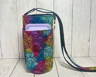 May include: A cylindrical fabric water bottle carrier featuring a vibrant rainbow-colored fan pattern. The carrier includes a long black adjustable shoulder strap and a small exterior pocket containing a light purple rectangular plastic lid.