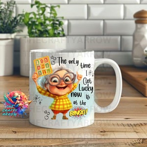 May include: White ceramic mug with a cartoon illustration of a woman holding a bingo card. The text on the mug reads "The only time I get lucky now is at the Bingo!"
