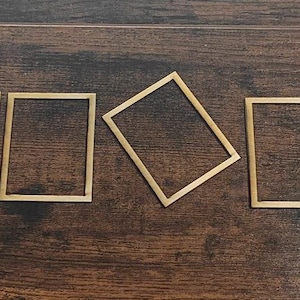 May include: A collection of eight small, rectangular wooden frames arranged on a dark wood surface. A yellow ruler is positioned on the right side, providing scale. The frames are light brown and appear to be unfinished.