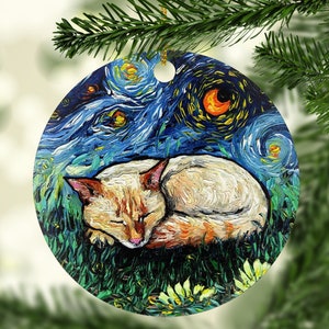 May include: A white cat with orange markings is sleeping in a field of green grass. The background is a blue and yellow starry night sky, reminiscent of Vincent van Gogh's "Starry Night". This is a round, painted ornament.