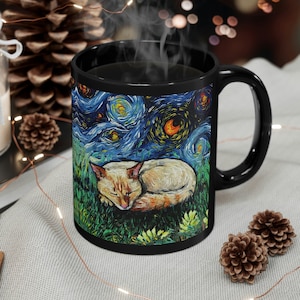 May include: Black ceramic coffee mug with a white cat sleeping on a green field with a starry night sky background. The mug has a white rim and handle.