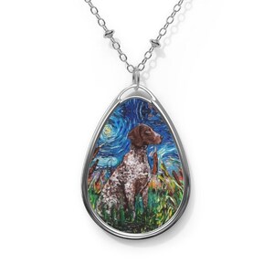 May include: Silver-toned necklace with a pendant featuring a dog in a field under a starry night sky. The oval pendant has a silver border and a chain with small, round beads. The dog is brown and white, and the artwork is reminiscent of Van Gogh's style.