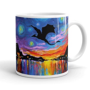 May include: A white ceramic mug with a colorful painting of a silhouette of a dragon flying over a city skyline at sunset. The sky is a vibrant blue with yellow, orange, and purple clouds. The city lights are reflected in the water below.