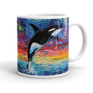 K&ouml;nnte beinhalten: Wei&szlig;e Keramiktasse mit einem farbenfrohen Gem&auml;lde eines Orcas, der aus dem Wasser springt, vor einem Hintergrund eines sternenklaren Nachthimmels.