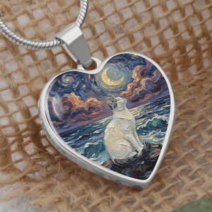 May include: Heart-shaped pendant with a silver chain. The pendant features a painting of a white cat gazing at a moonlit sky over the ocean. The artwork is in the style of Van Gogh, with swirling blues, oranges, and yellows.