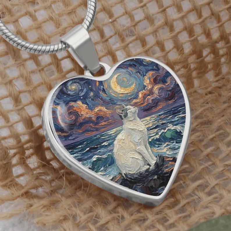 May include: Heart-shaped pendant with a silver chain. The pendant features a painting of a white cat gazing at a moonlit sky over the ocean. The artwork is in the style of Van Gogh, with swirling blues, oranges, and yellows.