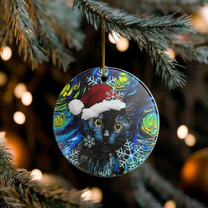 Pu&ograve; includere: Una decorazione rotonda in ceramica raffigurante un gatto nero con un cappello da Babbo Natale rosso e bianco. Lo sfondo presenta un motivo impressionista vorticoso blu, giallo e verde con illustrazioni di fiocchi di neve bianchi.