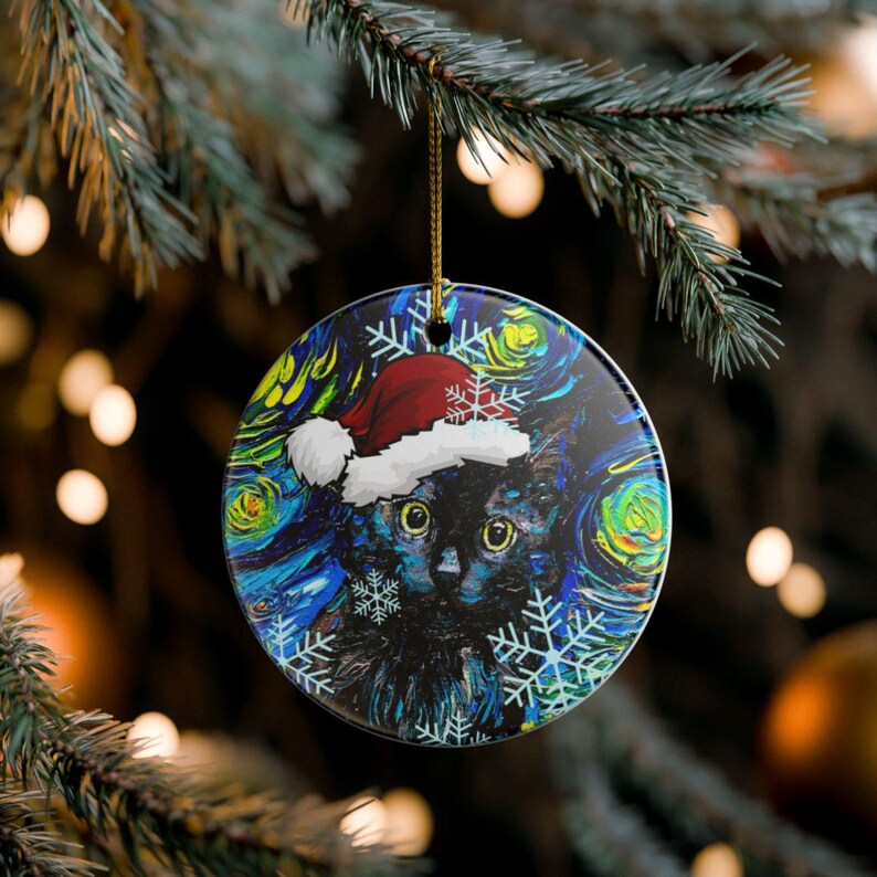 Pu&ograve; includere: Una decorazione rotonda in ceramica raffigurante un gatto nero con un cappello da Babbo Natale rosso e bianco. Lo sfondo presenta un motivo impressionista vorticoso blu, giallo e verde con illustrazioni di fiocchi di neve bianchi.