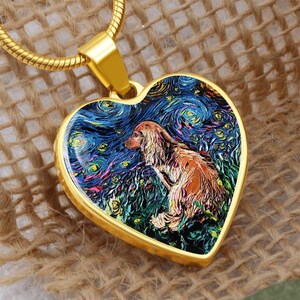 Op de afbeelding: Een goudkleurige hartvormige hanger met een hondenportret in de stijl van Van Goghs "Starry Night". De hanger hangt aan een gouden ketting. De hond is afgebeeld in bruin- en oranje tinten, tegen een wervelende blauw-gele achtergrond.