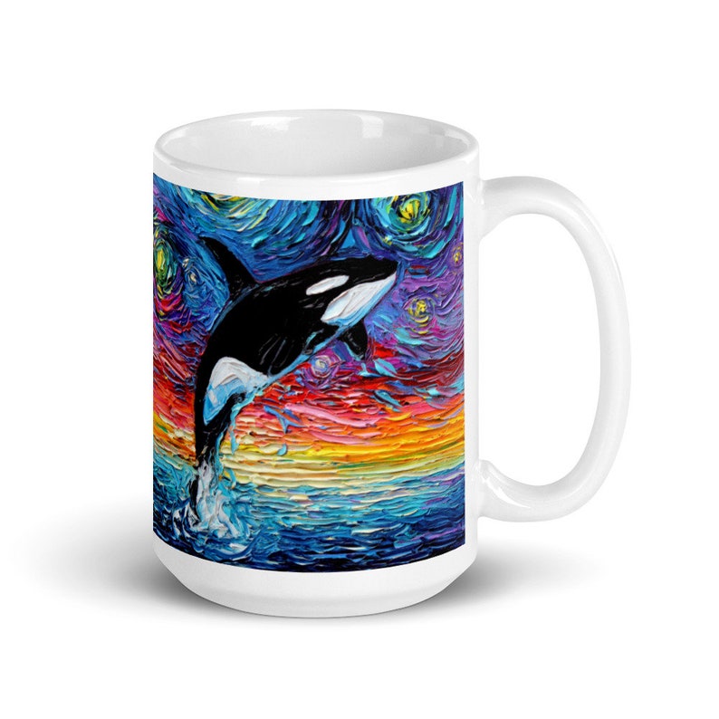 K&ouml;nnte beinhalten: Wei&szlig;e Keramiktasse mit einem farbenfrohen Gem&auml;lde eines Orcas, der aus dem Wasser springt, vor einem Hintergrund eines sternenklaren Nachthimmels.