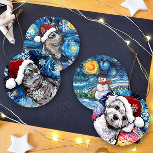Pu&ograve; includere: Tre decorazioni natalizie rotonde con disegni artistici. Due decorazioni mostrano cani che indossano cappelli da Babbo Natale rossi e bianchi, e una decorazione raffigura un pupazzo di neve. Tutti i disegni presentano uno sfondo blu vorticoso.