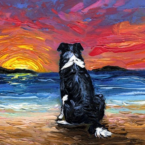 May include: A black and white border collie dog sits on a sandy beach, looking out at a colorful sunset over the ocean. The sky is a mix of pink, orange, and purple, with a bright yellow sun setting in the distance.