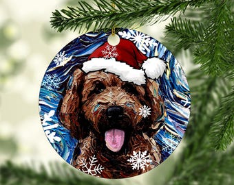 May include: A round ceramic ornament featuring a textured, impasto-style painting of a brown dog wearing a red and white Santa hat. The background is a swirling blue pattern with white snowflake icons scattered across the surface of the ornament.