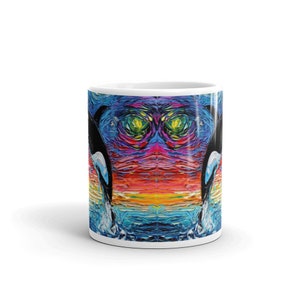 K&ouml;nnte beinhalten: Eine wei&szlig;e Keramiktasse mit einem farbenfrohen abstrakten Design von zwei Orcas, die aus dem Wasser springen. Das Design zeigt einen Regenbogen aus Farben, darunter Blau, Gr&uuml;n, Gelb, Orange, Rot und Lila.
