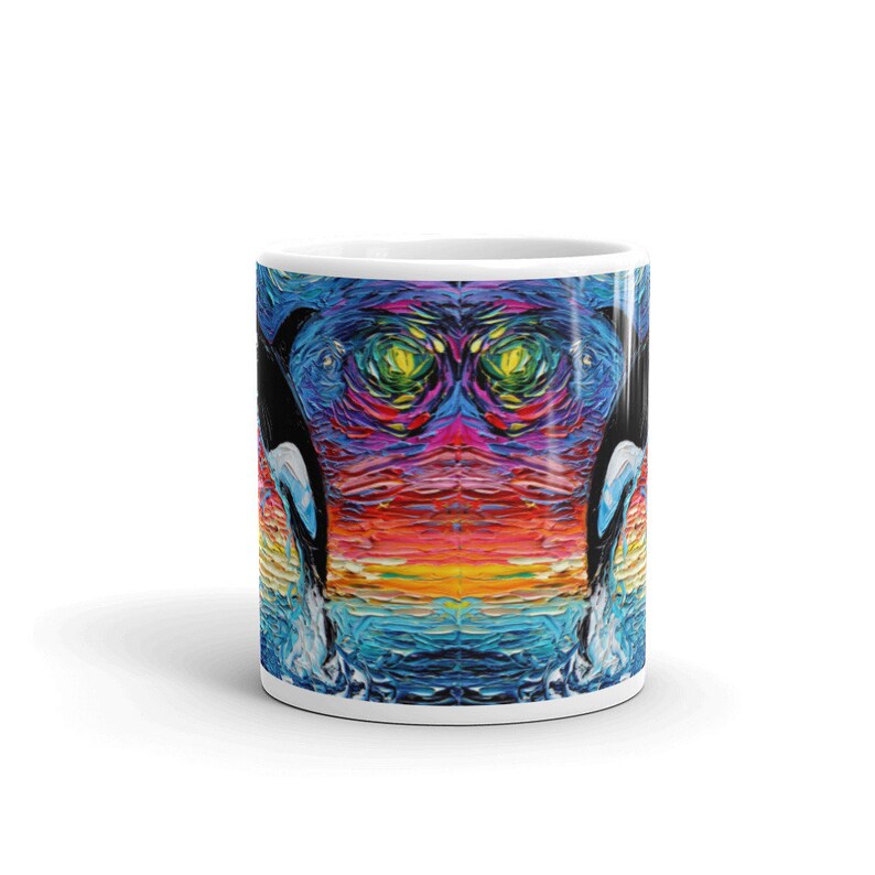 K&ouml;nnte beinhalten: Eine wei&szlig;e Keramiktasse mit einem farbenfrohen abstrakten Design von zwei Orcas, die aus dem Wasser springen. Das Design zeigt einen Regenbogen aus Farben, darunter Blau, Gr&uuml;n, Gelb, Orange, Rot und Lila.