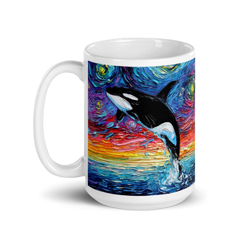 K&ouml;nnte beinhalten: Wei&szlig;e Keramiktasse mit einem farbenfrohen Gem&auml;lde eines Orcas, der aus dem Wasser springt, vor einem Hintergrund eines sternenklaren Nachthimmels.