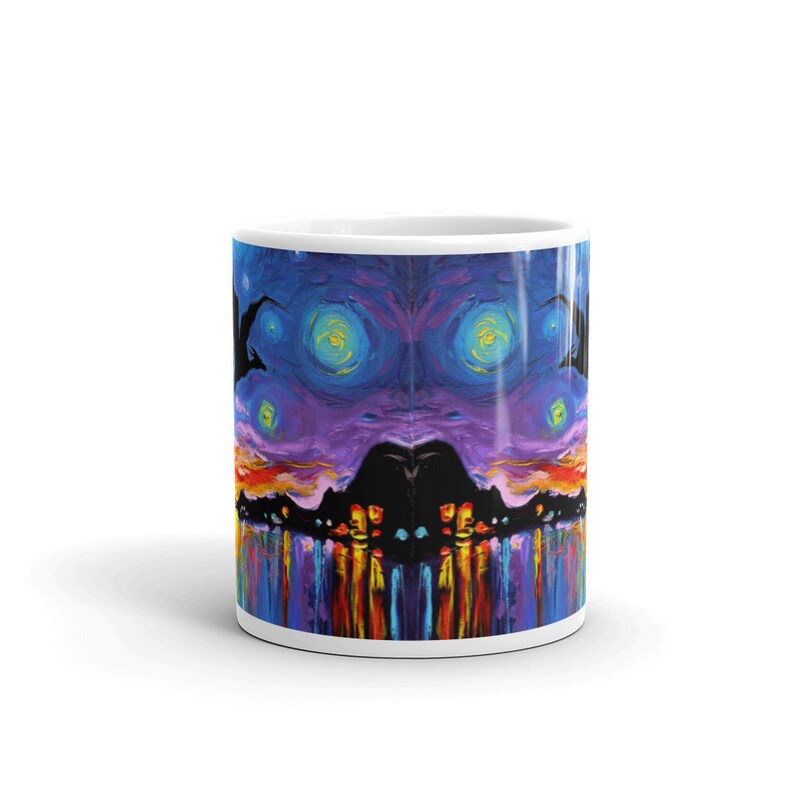 May include: White ceramic mug with a colorful abstract design. The design features a purple and blue background with yellow and orange accents. The design is symmetrical and appears to be a reflection of itself.