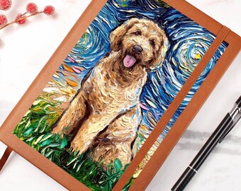 May include: A brown leather journal featuring a painting of a golden doodle dog in the style of Van Gogh's "Starry Night." The dog is depicted with its tongue out, set against a swirling blue and yellow sky and green grass.