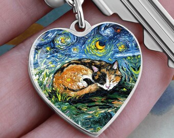 Peut inclure: Pendentif en forme de cœur argenté avec un chat calico endormi sur un fond de ciel étoilé, inspiré du style de Van Gogh. Le pendentif est attaché à un porte-clés.