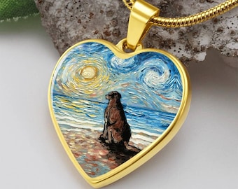 Peut inclure: Collier pendentif en forme de cœur doré. Le pendentif représente une peinture d'un chien brun assis sur une plage, avec un ciel étoilé et un arrière-plan océanique. Le collier a une chaîne dorée.