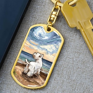 May include: A gold-colored dog tag with a West Highland White Terrier illustration on a beach scene, with a sky and ocean background. The tag is attached to a gold keychain and a gold key.