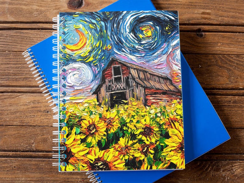 May include: A spiral-bound notebook featuring a vibrant painting of a barn in a field of sunflowers under a starry night sky. The notebook is set against a blue notebook on a wooden surface.