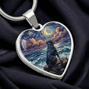 May include: Heart-shaped pendant with a silver chain. The pendant features a painting of a dog sitting on a rock, gazing at a starry night sky over the ocean. The artwork uses blues, oranges, and yellows.