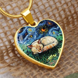 Könnte beinhalten: Goldfarbener herzförmiger Anhänger mit einem schlafenden Katzendesign. Der Anhänger zeigt ein Gemälde einer Katze, die im Gras unter einem Sternenhimmel ruht. Der Anhänger hängt an einer goldenen Kette.