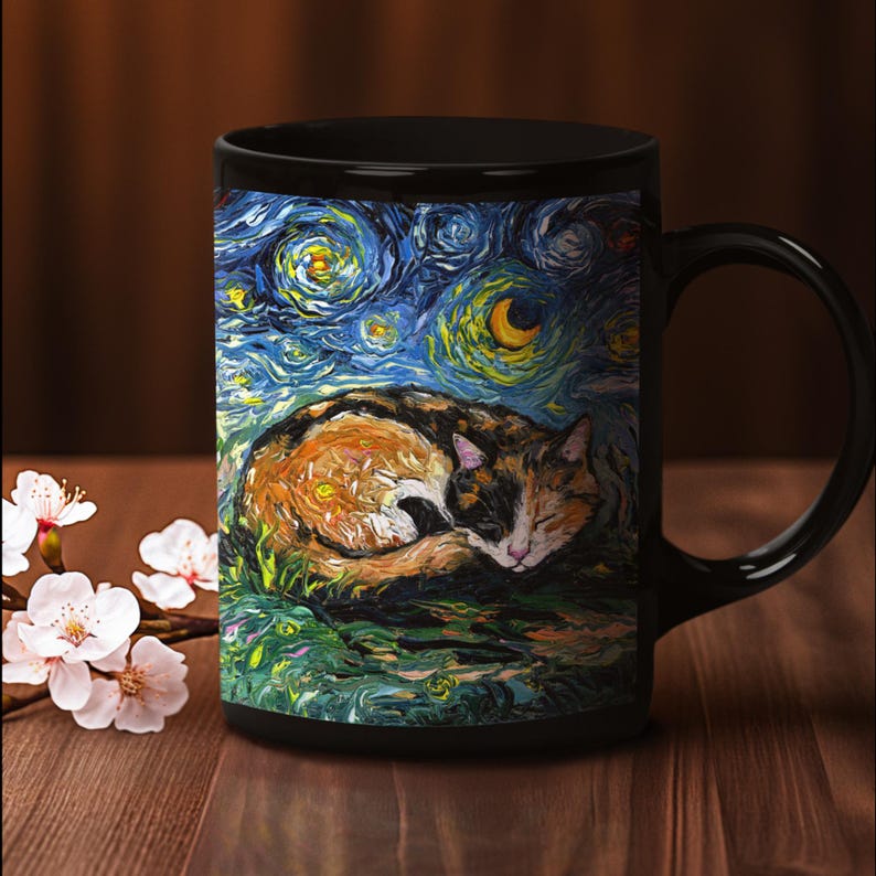 May include: Black ceramic mug with a colorful painting of a calico cat sleeping on a green field under a starry night sky. The painting is reminiscent of Vincent van Gogh's Starry Night.