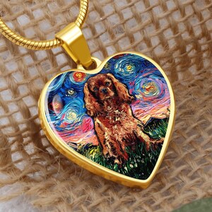 May include: Gold-toned heart-shaped pendant with a dog portrait in the style of Van Gogh's "Starry Night." The pendant hangs from a gold chain. The dog is brown and the background features swirling blues, oranges, and yellows.