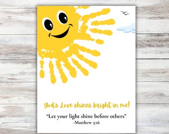 May include: A white print featuring a smiling yellow sun made of handprints. The text "God's Love shines bright in me!" and a Bible verse are below the sun. Two birds and a cloud are in the upper right corner.