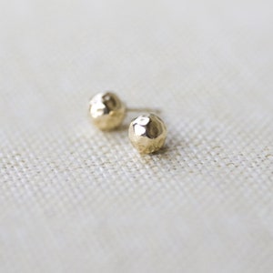 May include: A pair of gold hammered ball stud earrings. The earrings are small and round, with a textured surface.