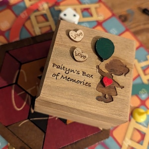 May include: A wooden memory box with the inscription "Paityn's Box of Memories". The lid is decorated with a cutout of a girl holding a green balloon and two small wooden hearts with the word "Love".