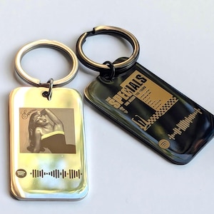 May include: Two silver keychains with black rings. One keychain features a black and gold design with the text "The Specials" and a Spotify barcode. The other keychain features a silver design with a black and white image of a woman and a Spotify barcode.
