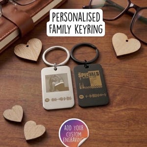 May include: Two rectangular metal keyrings with split rings, one silver and one black. The silver keyring features a monochrome photo and a Spotify code. The black keyring displays The Specials album art and a Spotify code. Text reads: PERSONALISED FAMILY KEYRING and ADD YOUR CUSTOM ENGRAVING.